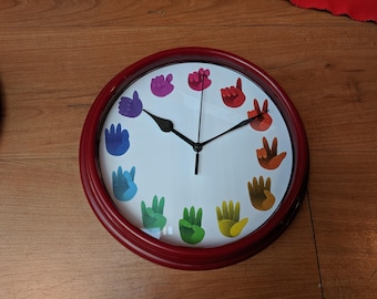 May include: A red circular clock with a white face and black hands. The clock face features a rainbow of hands in different positions.