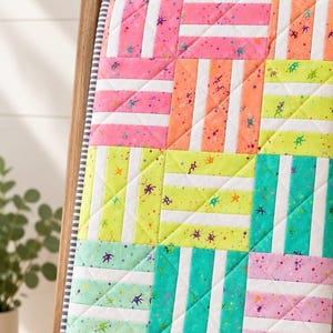 May include: A quilted blanket featuring a grid of square blocks, each composed of alternating solid white strips and neon-colored fabric strips in pink, orange, lime green, teal, and purple, all decorated with small, dark, star-like speckles.