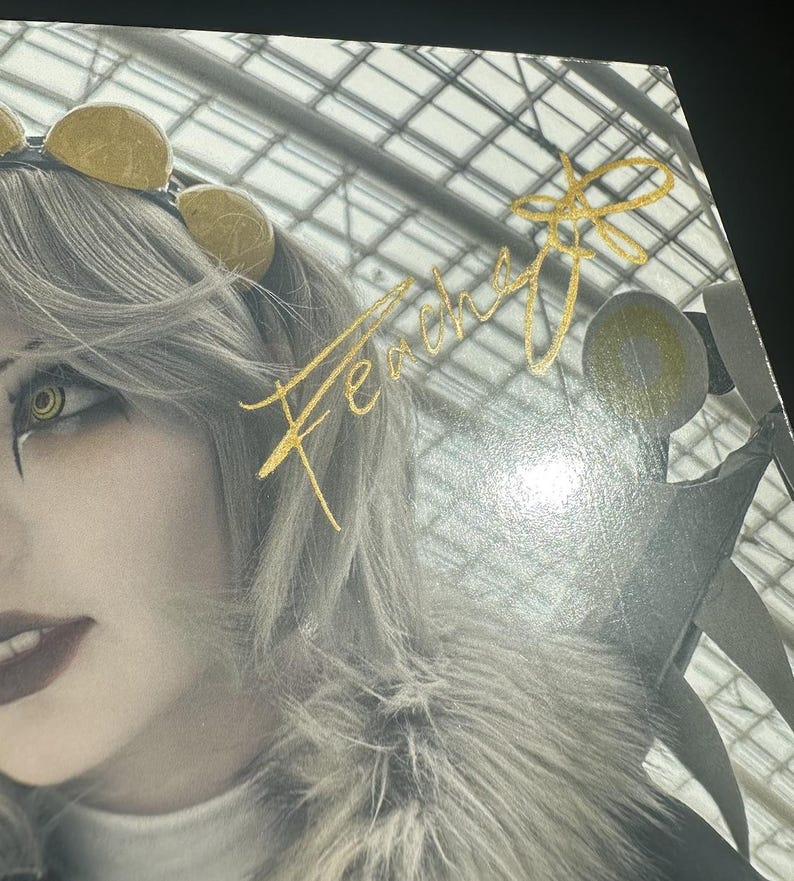 May include: A close-up of a woman's face with a gold headband and a gold signature that says "Fercha" on a white background.