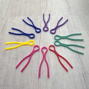 Peut inclure: Un ensemble de dix élastiques à cheveux colorés dans différentes couleurs, notamment bleu, violet, jaune, vert et rose. Les élastiques à cheveux sont disposés en cercle sur une surface en bois clair.