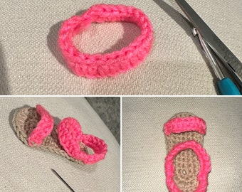 Op de afbeelding: Een close-up van een handgemaakte gehaakte babysandaal in lichtbruin met felroze accenten. De sandaal heeft een roze bandje en een roze band om de enkel. Een schaar en een haaknaald zijn op de achtergrond te zien.