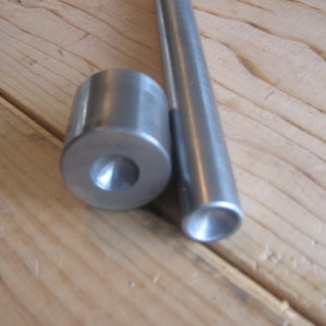 May include: Two metal tools for leather crafting. One is a round, silver punch with a pointed tip. The other is a long, silver rod with a rounded end.