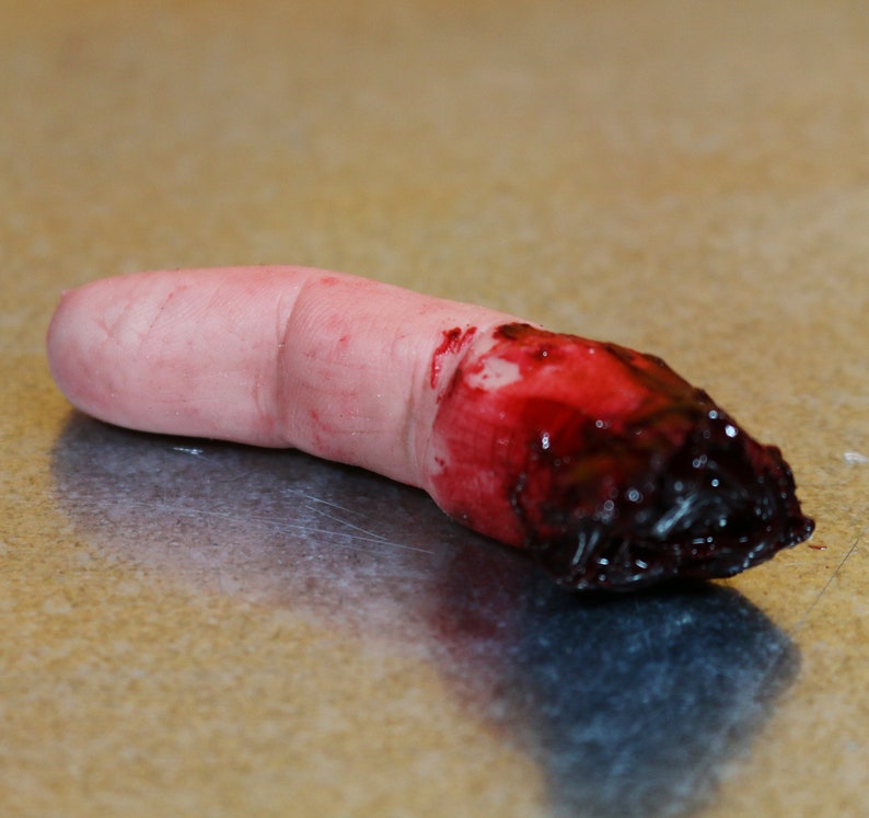 Peut inclure: Un doigt factice avec une blessure sanglante r&eacute;aliste &agrave; l'extr&eacute;mit&eacute;. Le doigt est de couleur chair avec une texture de peau d&eacute;taill&eacute;e, et la blessure est d'un rouge profond avec du sang caill&eacute; fonc&eacute;.