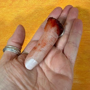 May include: A realistic severed finger prop with a white painted fingernail and a bloody, torn end. The prop is designed to look like a real finger and is likely used for Halloween or horror-themed events.