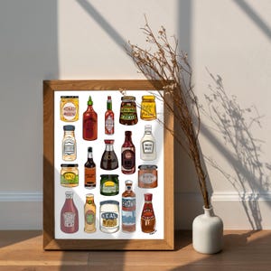 May include: A framed print featuring a collection of illustrated condiment bottles and jars. The artwork includes various sauces, mustards, and pickles, with labels like "BBQ," "Soy Sauce," and "Original Pickles." The print is displayed on a wooden surface.