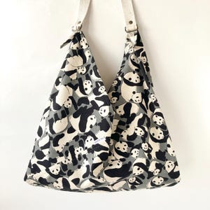 May include: A large, gray and white tote bag with a panda print. The bag has white straps and a small white label that says "Cotton & Silk".