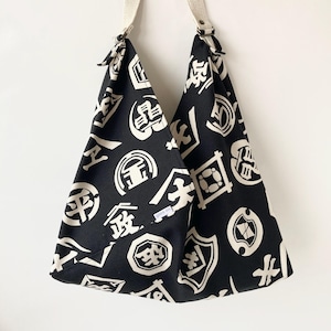 May include: Black and white tote bag with a Japanese pattern of white kanji characters on a black background. The bag has a long strap and is made of a sturdy fabric.