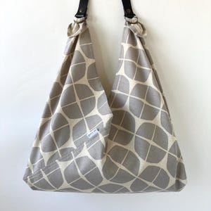 May include: A gray and cream-colored tote bag with a geometric leaf pattern. The bag has black leather straps and a small pocket with a white tag that reads "goons on". The bag is made of fabric.