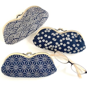 May include: Three elongated fabric spectacle cases with brass-toned metal kiss-lock closures. Each case features a distinct dark blue and white pattern: one with concentric waves, one with small floral motifs, and one with a geometric star design.