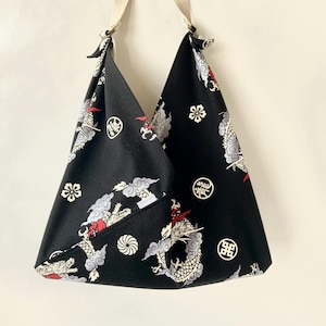May include: A black fabric tote bag with a white and red dragon design. The bag has a white strap and a white and red floral pattern.