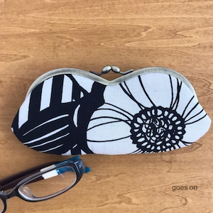 May include: A fabric glasses case featuring a black and white floral pattern, with a metal clasp. The case has a large flower design. The text "goes on" is visible in the lower right corner.