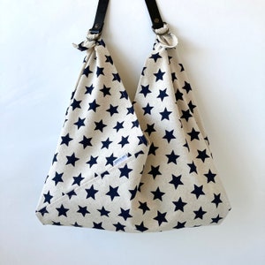 May include: A beige tote bag with a navy blue star pattern. The bag has black leather straps and metal rings. The text "goes on" is visible on the side of the bag.