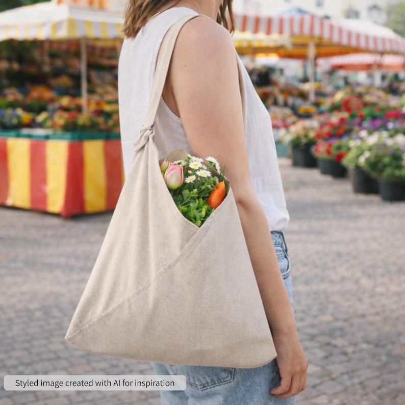 May include: A beige canvas hobo bag with a single shoulder strap and a triangular folded design, containing a bouquet of fresh flowers including pink tulips, white daisies, and orange blossoms, worn over the shoulder with a white tank top.