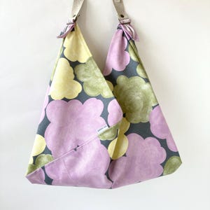 May include: A large, gray tote bag with a floral pattern in shades of yellow, green, and purple. The bag has a small pocket on the front with the text "goods on" printed on it.