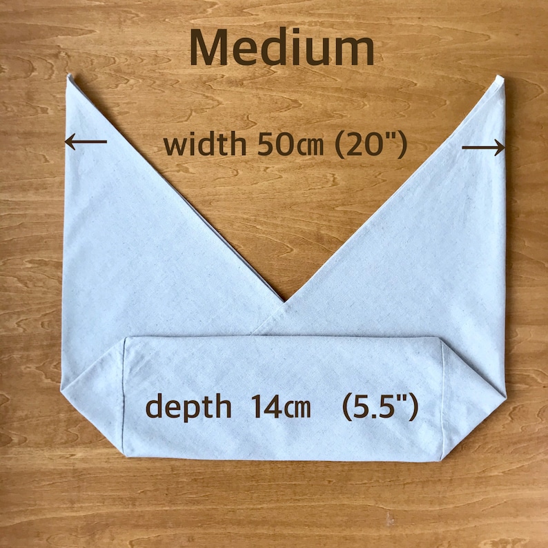 May include: A medium-sized off-white fabric bag with a V-shaped top opening. The text Medium is printed at the top. Arrows indicate a width of 20 inches, and text specifies a depth of 5.5 inches. The bag is laid flat against a wooden surface.