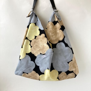 May include: A black tote bag with a large floral print in shades of yellow, brown, and gray. The bag has leather straps and a small white label that says "goss on".