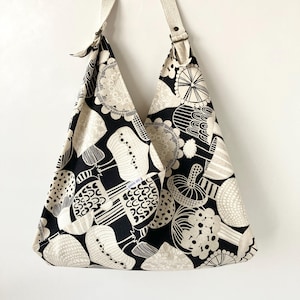 May include: A black and white tote bag with a mushroom print. The bag has a long strap and is made of a sturdy fabric.