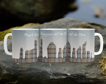 May include: Three white ceramic mugs with a blue and brown plaid design. The mugs feature a silhouette of the Old Man of Storr rock formation on the Isle of Skye, Scotland. The text "People Disappear All The Time" is printed on the mugs.