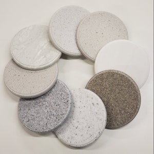 May include: Eight round, white, gray, and brown coasters with a speckled pattern. The coasters are arranged in a circle on a white surface.