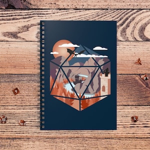 May include: A spiral-bound notebook with a dark blue cover featuring a fantasy landscape design inside a geometric shape. The design includes a dragon, mountains, a waterfall, and a castle. Several dice are scattered around the notebook.