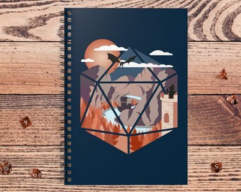 May include: A spiral-bound notebook with a dark blue cover featuring a fantasy landscape design inside a geometric shape. The design includes a dragon, mountains, a waterfall, and a castle. Several dice are scattered around the notebook.