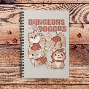 May include: Spiral-bound notebook with the text "DUNGEONS DOGGOS" and illustrations of cartoon dogs dressed as fantasy characters. The dogs are various shades of brown and tan, with red and brown accents. Several red dice are scattered around the notebook.