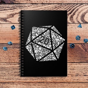 May include: A black spiral notebook with a white 20-sided die design. The die is filled with smaller white designs. The notebook is on a wooden surface with blue dice scattered around it.
