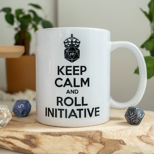 May include: White ceramic mug with a black design that says "Keep Calm and Roll Initiative" with a black and white illustration of a 20-sided die with a crown on top.
