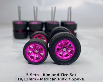 Peut inclure: Cinq ensembles de roues de voiture miniature à l'échelle 10/12 mm avec des pneus noirs et des jantes roses. Les jantes ont un design à 7 branches. Le texte "1:64 Scale Wheels" et "5 Sets - Rim and Tire Set 10/12mm - Mexican Pink 7 Spoke." est visible sur l'image.