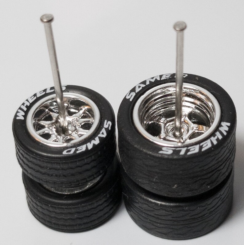 May include: Two sets of four chrome wheels with black tires. Each set has a silver metal rod going through the center of the wheels. The wheels have white lettering that reads 'WHEELS' and 'SAME'.