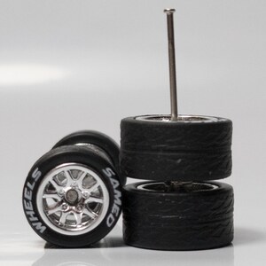 May include: Two sets of black rubber tires with silver rims. The tires have a tread pattern and the rims have the words 'WHEELS' and 'SAMED' printed on them. A silver metal pin is sticking out of the top of the tires.