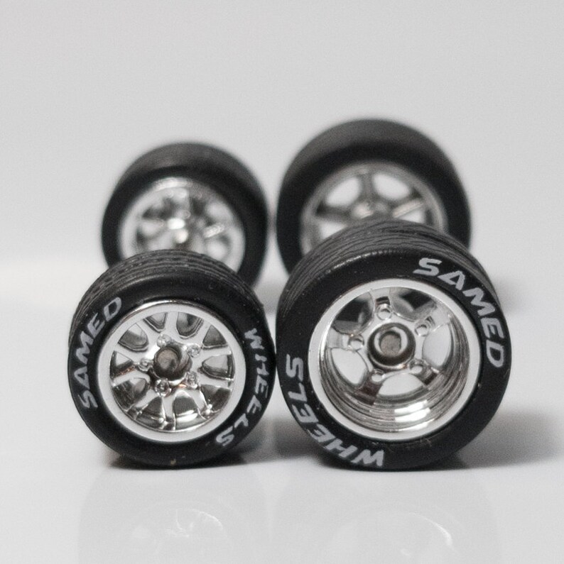 May include: Four silver chrome wheels with black tires. The tires have white lettering that reads 'WHEELS' and 'SAMED'.
