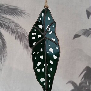 Puede incluir: Un adorno de hoja de vidrio coloreado con un dise&ntilde;o de manchas verdes y blancas. La hoja est&aacute; colgada de una cuerda.