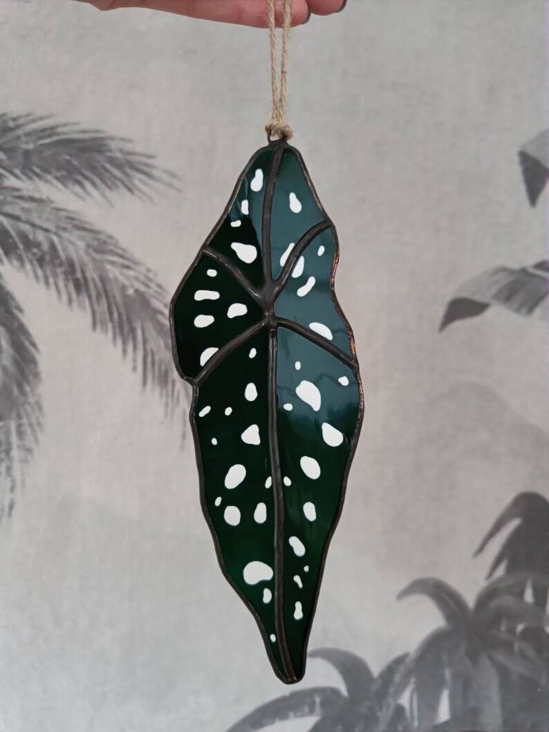 Puede incluir: Un adorno de hoja de vidrio coloreado con un dise&ntilde;o de manchas verdes y blancas. La hoja est&aacute; colgada de una cuerda.