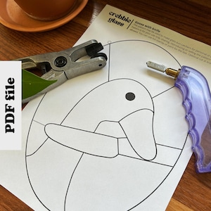 Op de afbeelding: Een zwart-witte lijntekening van een gans op een wit vel papier. Het papier wordt omringd door een glascutter, een glascuttergereedschap en een tang. De tekst "Goose with knife" is op het papier gedrukt. De tekst "crebbie glass" is op het papier gedrukt.