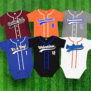 Könnte beinhalten: Sechs Baby-Baseballtrikots in verschiedenen Farben mit unterschiedlichem Text und Zahlen. Die Trikots sind weiß, orange, grau, blau, schwarz und rot. Der Text auf den Trikots lautet "Custom Text", "It's a Boy!", "Team Name", "Personalized", "Wolverines" und "Southeast".