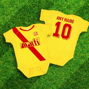 May include: Yellow baby bodysuit with a red diagonal stripe and the word "marfi" in a red box. The bodysuit has a red number "10" and the text "ANY NAME" on the back.