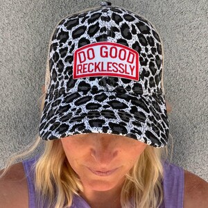 Op de afbeelding: Een pet met een zwart, wit en grijs luipaardprint ontwerp op het voorpaneel en de klep. De pet heeft een rood embleem met de witte tekst "DO GOOD RECKLESSLY". De achterkant is van beige mesh.