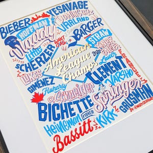 May include: Framed art print with a baseball theme. The design features player names in blue, red, and gold, with the words "American League Champs" in the center. The print is set against a white background, with a dark frame.