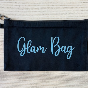 May include: Black canvas zippered pouch with a light blue inscription that reads "Glam Bag".