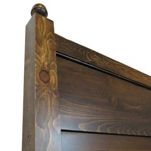 May include: A dark brown stained wooden headboard featuring horizontal planks and a square vertical post topped with a rounded finial. The wood grain is visible throughout the surface, showcasing natural knots and variations in the dark finish.
