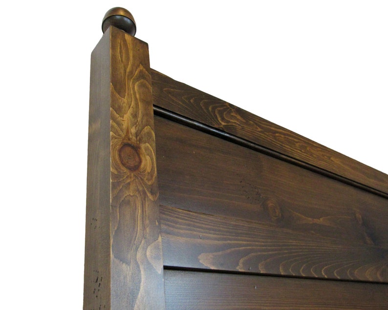 May include: A dark brown stained wooden headboard featuring horizontal planks and a square vertical post topped with a rounded finial. The wood grain is visible throughout the surface, showcasing natural knots and variations in the dark finish.