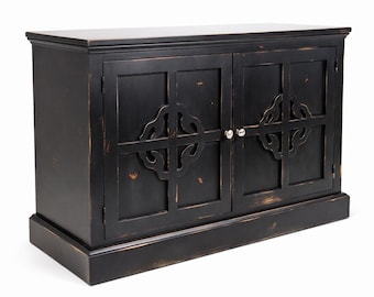 May include: A rectangular black wooden cabinet featuring two doors with a decorative cutout pattern and small silver knobs. The finish shows intentional distressed wear along the edges, revealing brown tones beneath the black paint.