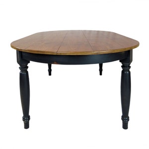 May include: A round dining table featuring a natural wood grain tabletop with a smooth finish and a black painted base. The table is supported by four turned legs with a distressed black paint finish, showing subtle wear along the edges.