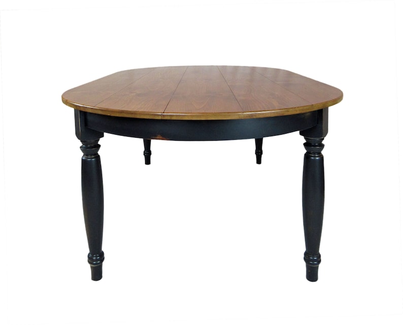 May include: A round dining table featuring a natural wood grain tabletop with a smooth finish and a black painted base. The table is supported by four turned legs with a distressed black paint finish, showing subtle wear along the edges.