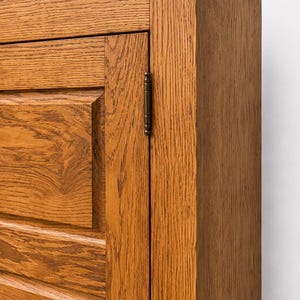 Corner detail of solid oak TV cabinet showing handcrafted joinery, frame construction, and wood grain.