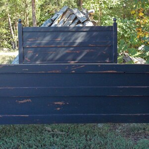 May include: A black wooden bed frame featuring a headboard and footboard with horizontal slats. The finish has a distressed appearance, revealing brown wood tones along the edges and surfaces of the posts and panels, topped with spherical finials.