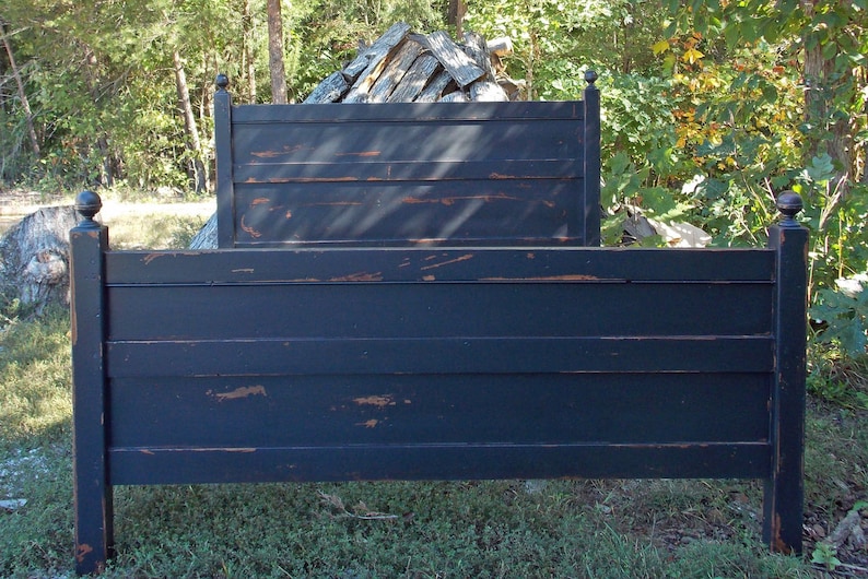 May include: A black wooden bed frame featuring a headboard and footboard with horizontal slats. The finish has a distressed appearance, revealing brown wood tones along the edges and surfaces of the posts and panels, topped with spherical finials.