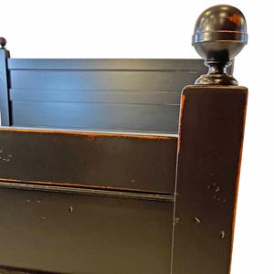 May include: A black wooden bed frame featuring a headboard with horizontal slats and a square corner post topped with a large spherical finial. The dark finish shows signs of wear along the edges, revealing a lighter brown tone underneath.