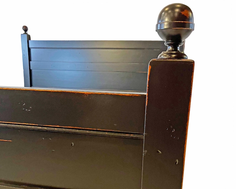 May include: A black wooden bed frame featuring a headboard with horizontal slats and a square corner post topped with a large spherical finial. The dark finish shows signs of wear along the edges, revealing a lighter brown tone underneath.